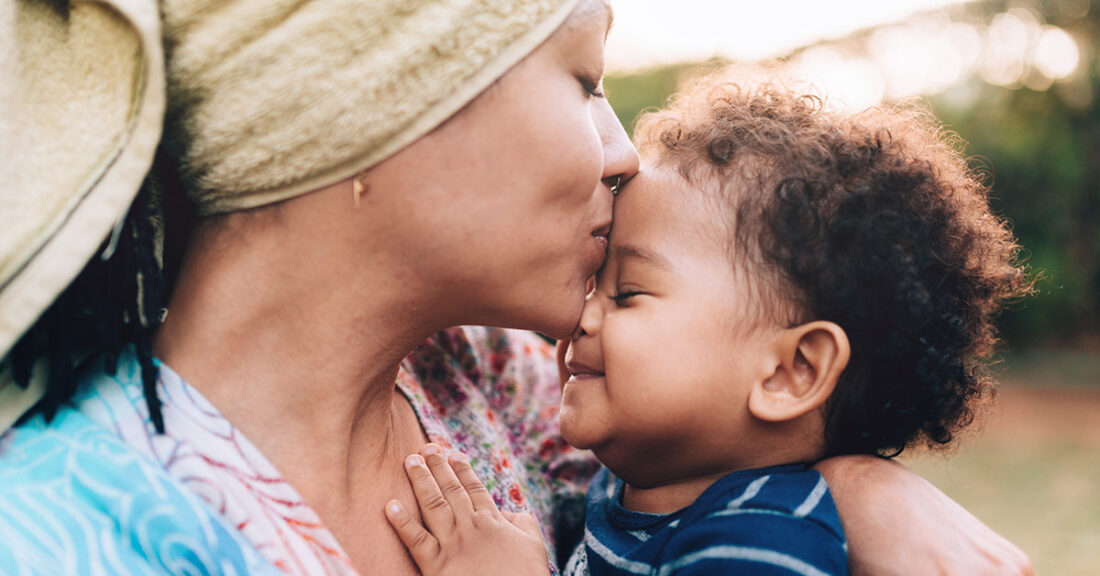 A mom gives her infant a kiss on the forehead.