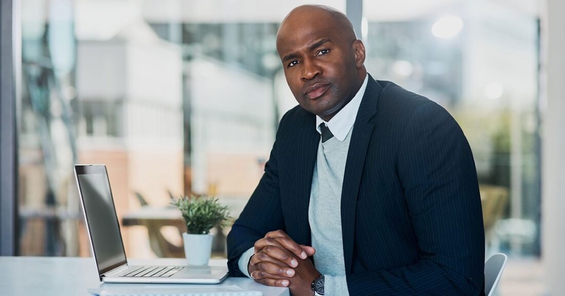 An African American man sits at a desk, facing a computer