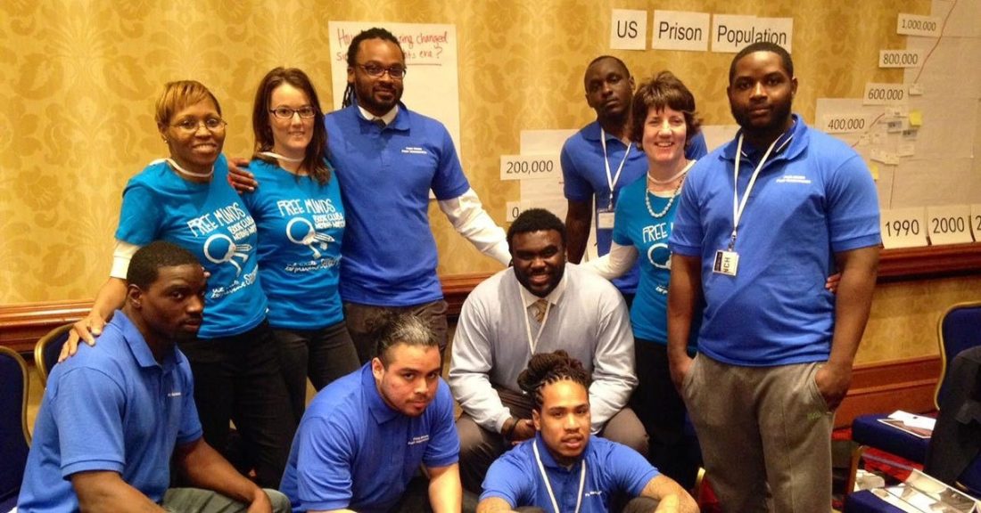 Ten people, most in blue T-shirts, are grouped together and smiling and looking at the camera.