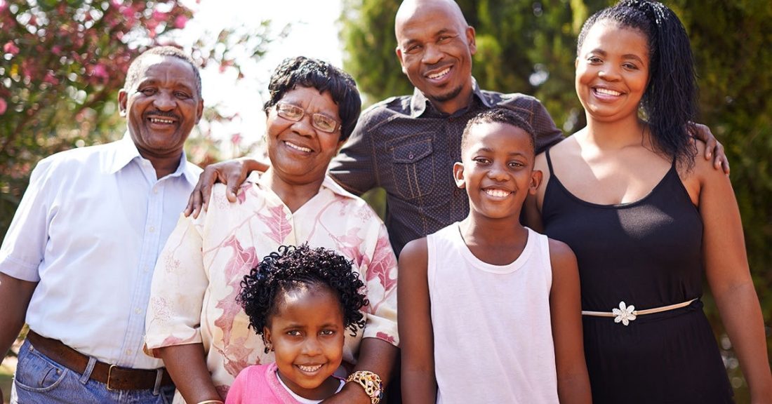 A multigenerational Black family poses together, smiing, outdoors