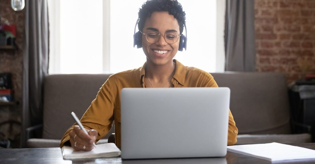 Young Black woman sits at a laptop and smiles while she takes notes about youth mental health.