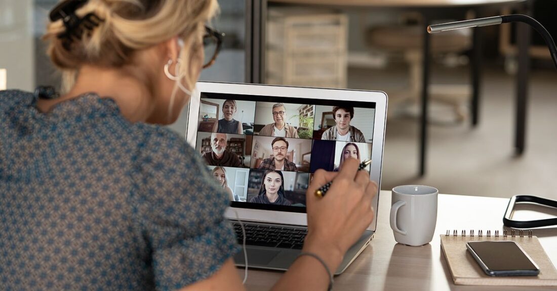 Woman in office setting looks at a computer screen, which depicts a collection of other individuals participating in a virtual meeting