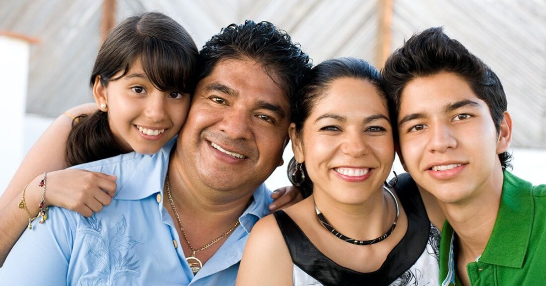 A Latino family of four, including an older boy and younger girl, smile at the camera.