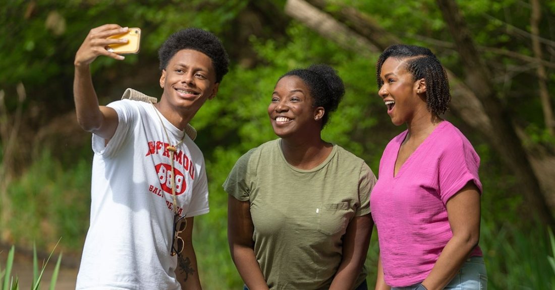 Three Black young people take a group selfie outdoors.