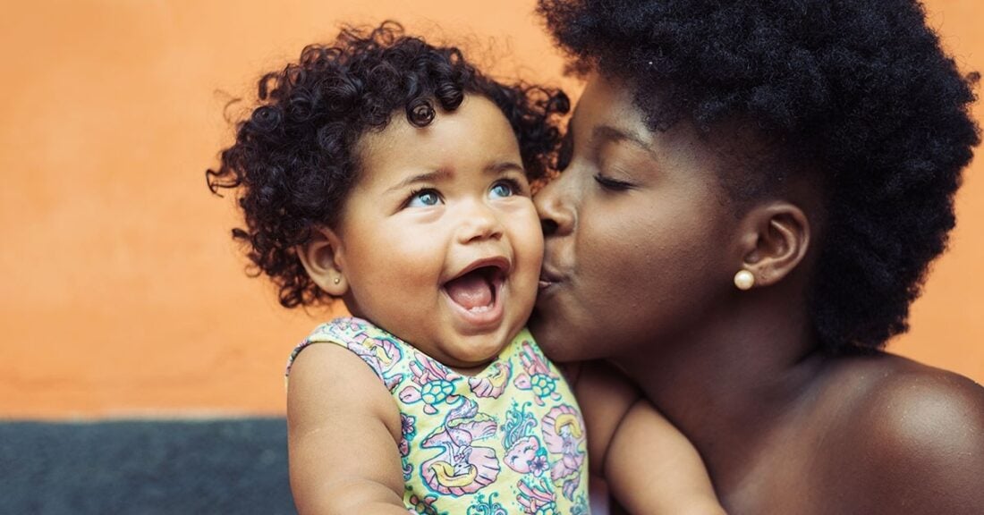 Black woman kisses a baby who is excited, smiling, with mouth open.