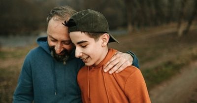 一位父亲和他十几岁的儿子都穿着连帽衫，一起在户外散步。父亲搂着儿子的肩膀，两人面带微笑。