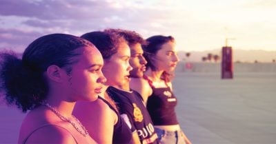 四个青少年站在海滩上。夕阳西下时，他们望向远方，脸上沐浴着阳光。