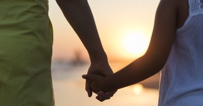 A silhouette of a mother and child holding hands amid a sunset.
