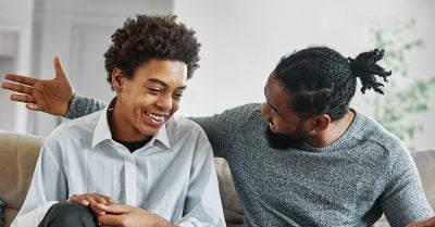 Two young black men sit on a couch, smiling