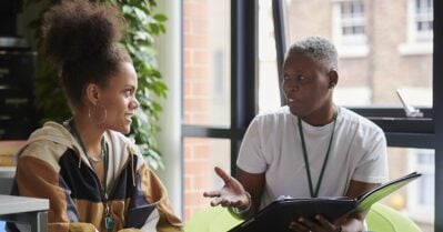 A young Black woman and an older Black woman sit together as they discuss a project.