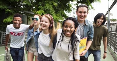 A diverse group of friends — all young people — smile while walking together outside.