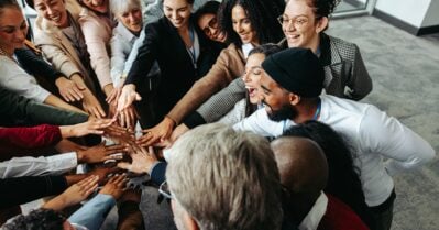 A diverse group of colleagues demonstrate teamwork and collaboration by putting their hands together during a corporate meeting.