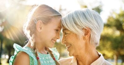 A little girl and her grandmother spend quality time in a park on a sunny day. They smile lovingly at each other.