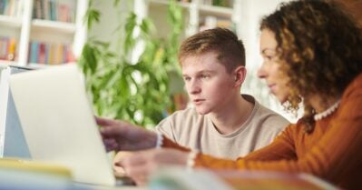 A young, adolescent boy sits with a female counselor, who points to something on a laptop.