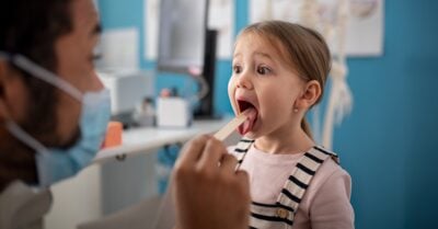 A young girl visits the doctor's office and gets her tonsils checked out by a medical professional.