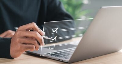 Person holding a pen next to a laptop, with a digital checklist overlay on the screen.