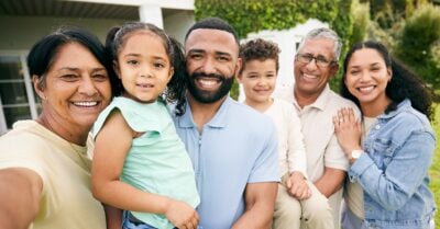 A multigenerational family picture showing six people--including two small children, two grandparents and two parents--standing outside, smiling at the camera.