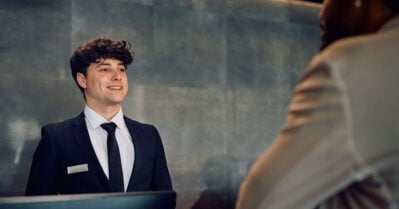 Happy young concierge talking to African American man who is checking in at the hotel.