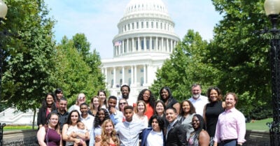 A diverse group of young leaders and adults pose together in front of the U.S. Capitol Building, representing youth engagement and advocacy efforts.