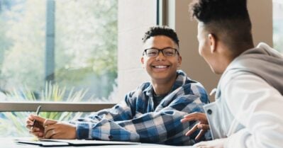 Waiting for class to start, a teenage boy smiles as he listens to his teen friend tell a story.