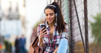 Teen girl with ponytail and headphones uses her smartphone outside