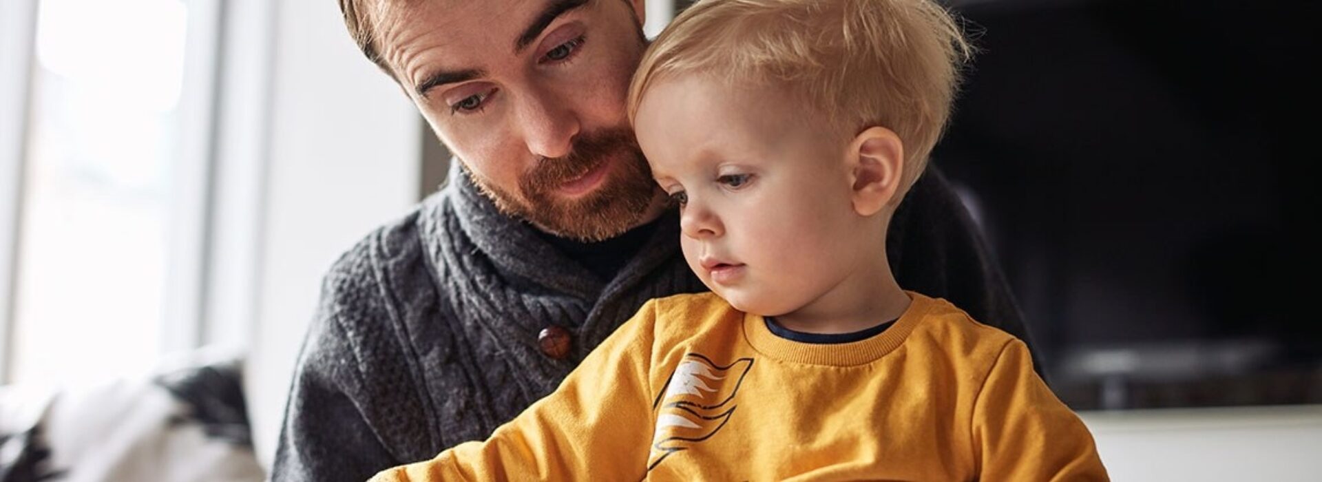 White father with goatee holds young son in yellow sweatshirt