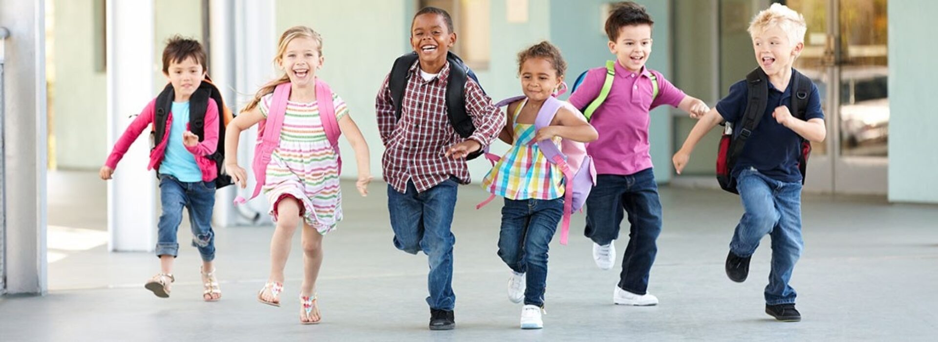 Six children with backpacks are running in a school building