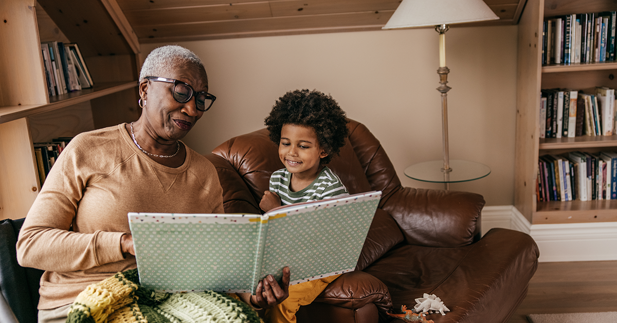 A black grandmother reads a book to her son in a cozy nook.