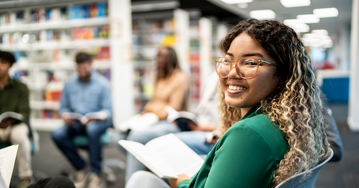 Young woman in green shirt and glasses is sitting in a bright library.