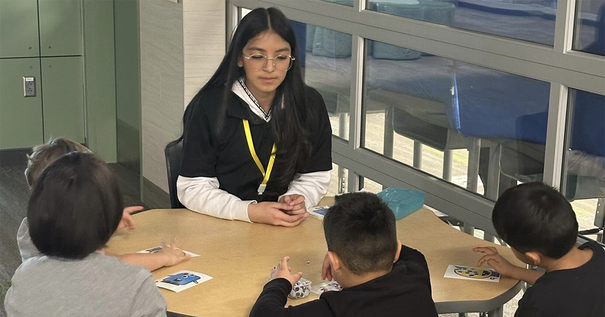 A young woman, who is a Latinos in Action participant, tutors younger students.