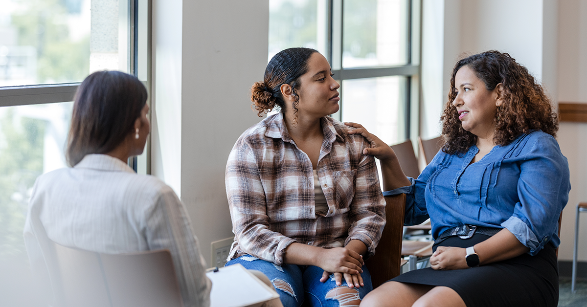 Three women sit in a circle, engaged in a supportive conversation during a group discussion.