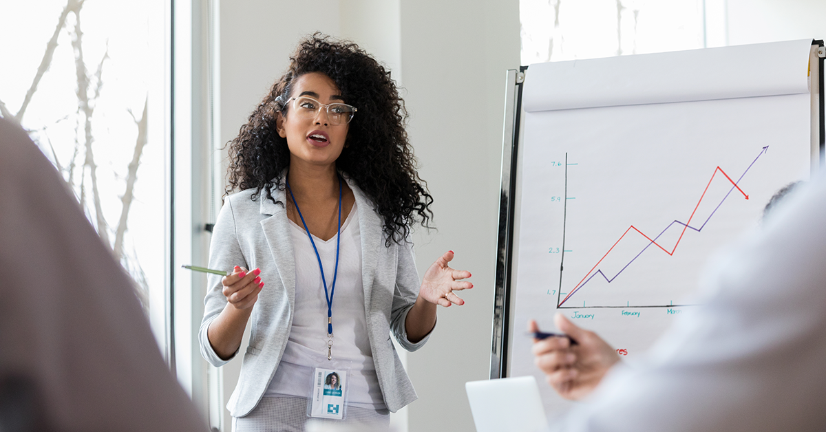 A Black professional woman stands in front of clipboard giving a presentation.