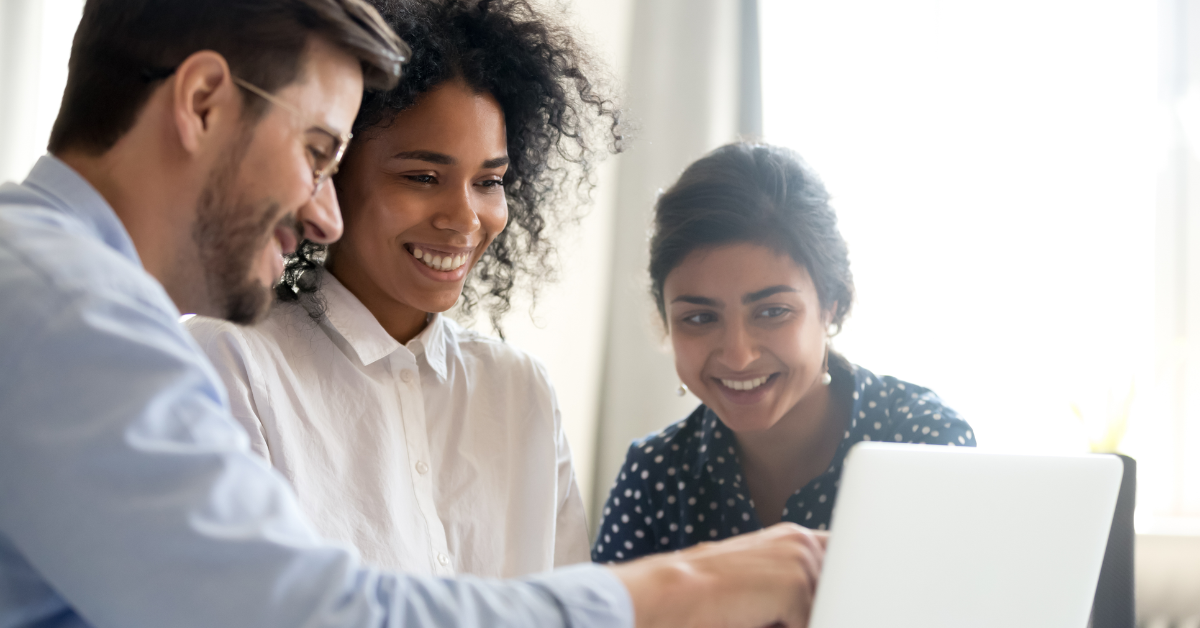 Three people sit around a laptop, looking at its screen and smiling.