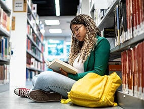 Young student woman sitting on ground at a community college library