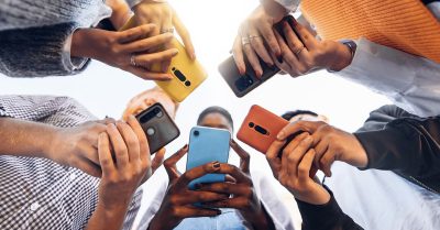Five people huddled in a circle checking out their cellphones. Their faces are obscured.
