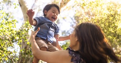 Woman throws her young son up in the air; the child is smiling
