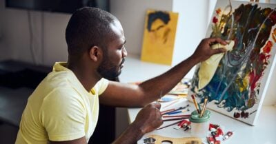 A black man is painting on a canvas in a studio.