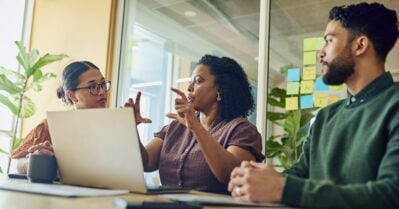 A diverse group of professionals brainstorm ideas while looking at a laptop in a modern office.