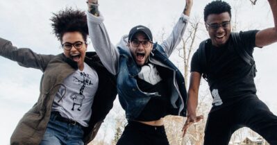 Three young people of color are outdoors and jumping for joy within the camera frame.