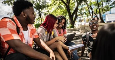 A group of Black teens smile and laugh while gathering in an outdoor setting.