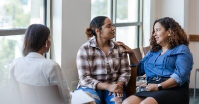 Three women sit in a circle, engaged in a supportive conversation during a group discussion.