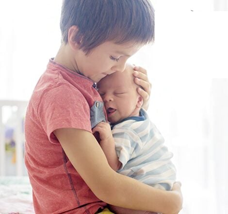 Young child gently holding and comforting a sleeping baby, conveying care, protection, and sibling bonding.