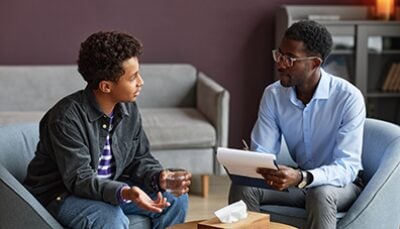 A young Black man speaks with a Black man in a supportive environment.
