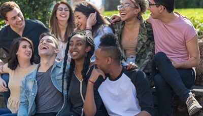 A multi-racial group of university students sit outside and smile and laugh.