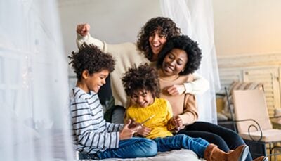 Two moms embrace each other as spend time with their son and daughter.